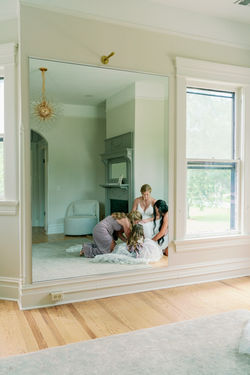 Bride being helped into her dress, reflected in a full-length mirror